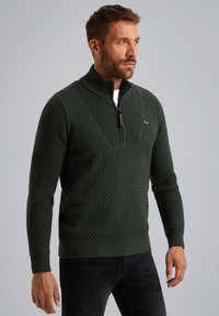 Dunkelgrüner Strickpullover mit einem Viertelreißverschluss-Kragen, strukturiertem Raute-Muster, gerippten Bündchen und Saum; verfügt über ein kleines Emblem auf der Brust.