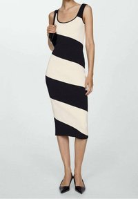 Abito lavorato a maglia con strisce diagonali nere e crema, sagoma aderente, scollatura a girocollo e spalline sottili, abbinato a décolleté nere a punta.