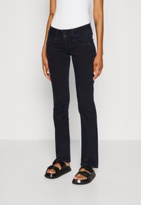 Tmavě modré zvonové džíny s pěti kapsami, zapínáním na knoflík a zip a jemnými švy; v kombinaci s černými sandály.