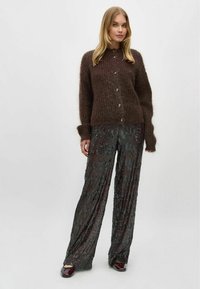 Cardigan tricotat maro cu închidere cu butoane, asociat cu pantaloni largi negri cu paiete și pantofi lucioși; materiale texturate și croială lejeră.