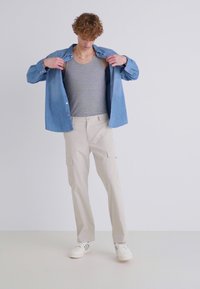 Camisa de mezclilla azul claro, camiseta de tirantes gris, pantalones cargo beiges con bolsillos y zapatillas blancas con rayas negras. Textura plana, corte informal.