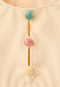 Gros plan sur un tissu côtes beige avec trois boutons irréguliers et brillants en vert, rose et crème, attachés verticalement.