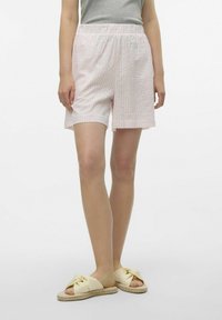Lichtroze en witte gestreepte shorts met een elastische tailleband, zittend boven de knie, gecombineerd met gele geknoopte slippers.