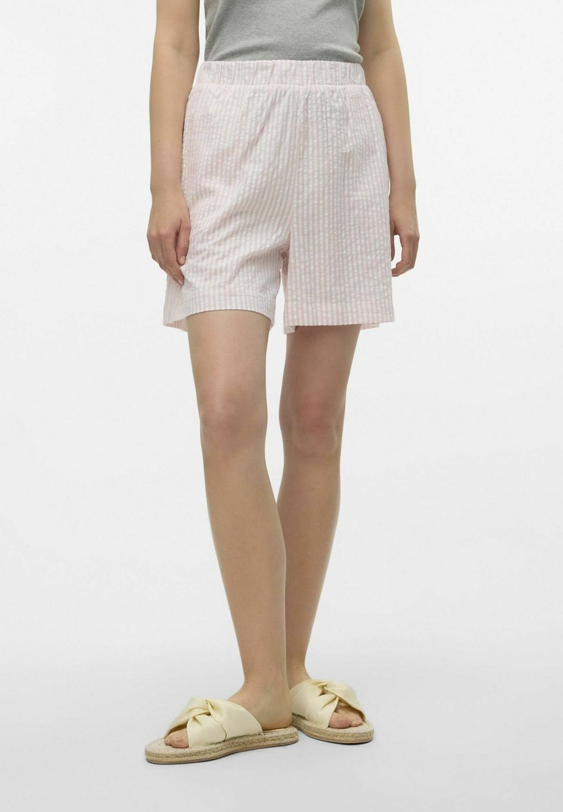 Lichtroze en witte gestreepte shorts met een elastische tailleband, zittend boven de knie, gecombineerd met gele geknoopte slippers.