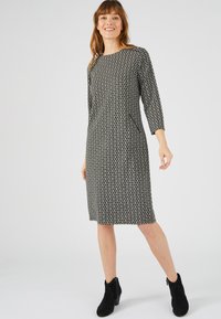 Vestito a modello nero e crema con motivo, fino al ginocchio con scollo rotondo e maniche a tre quarti, abbinato a stivali neri alla caviglia.