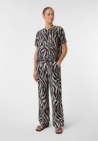 Bequemes zweiteiliges Outfit in Schwarz-und-Creme-Zebra-Print, aus leichtem Stoff gefertigt. Mit kurzen Ärmeln, elastischem Bund und Taschen.