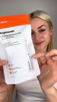 Rozjaśniające serum do oczu w białym opakowaniu z pomarańczową nakrętką; na przedzie widoczne są szczegóły produktu i instrukcje.