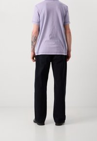 Fialové bavlněné tričko s kulatým výstřihem a krátkými rukávy. Vyznačuje se volnými tmavě modrými kalhotami a černými botami. Viditelné tetování na ruce.