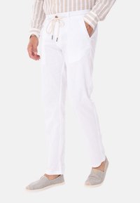 Pantaloni bianchi in lino con vita a cordoncino, tasche laterali e vestibilità rilassata, abbinati a scarpe espadrillas grigie con tomaia testurizzata.