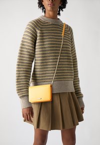 Stripet genser i beige og oliven nyanser, med ribbede mansjetter, sammen med en gul crossover-veske med kjede og enkel hardware.
