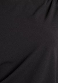 Gładka czarna tkanina z delikatnymi zagięciami i matową fakturą, ukazująca subtelne cienie i refleksy światła.