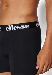 Schwarze Boxershorts mit einem schwarzen elastischen Bund, der mit dem weißen "ellesse" Logo verziert ist. Glatte Textur, taillierte Passform, mittelhoher Schnitt.
