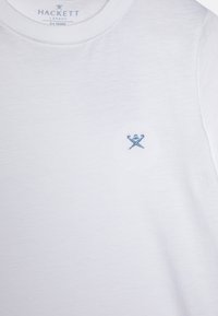 Hvit bomulls T-skjorte med rund hals og en liten blå brodert logo på brystet, passende for 3-4 år.