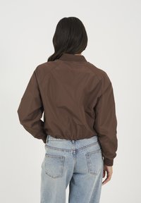 Brązowa kurtka bombowa z prążkowanym kołnierzem i elastycznym dołem, charakteryzująca się gładką powierzchnią i luźnym fasonem, w połączeniu z jasnoniebieskimi dżinsami.