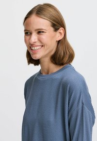 Blå randig långärmad topp med rund hals och neddragna axlar. Tyget har en strukturerad yta som skapar en avslappnad passform.