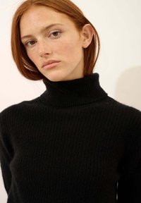 Czarny prążkowany sweter z golfem wykonany z dzianiny, z wysokim kołnierzem i dopasowanym krojem, o fakturowanej powierzchni.