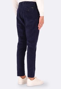 Pantaloni in corduroy blu navy con vestibilità affusolata, dotati di una tasca posteriore e un motivo a costine testurizzato. Abbinati a sneakers bianche.