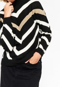 Jersey de rayas blancas y negras con un tejido texturizado, cuello alto y un patrón en zigzag dorado en las mangas.