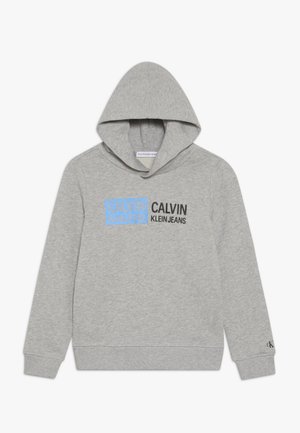 Sweat à capuche gris clair avec un logo Calvin Klein Jeans noir et bleu à l'avant, doté de manches longues et d'une poche frontale.