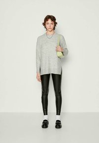 Grå strikkegenser, løs passform, v-hals; svarte faux skinn leggings; modellen bærer en grønn crossover-veske; svarte slip-on sko med hvite sokker.