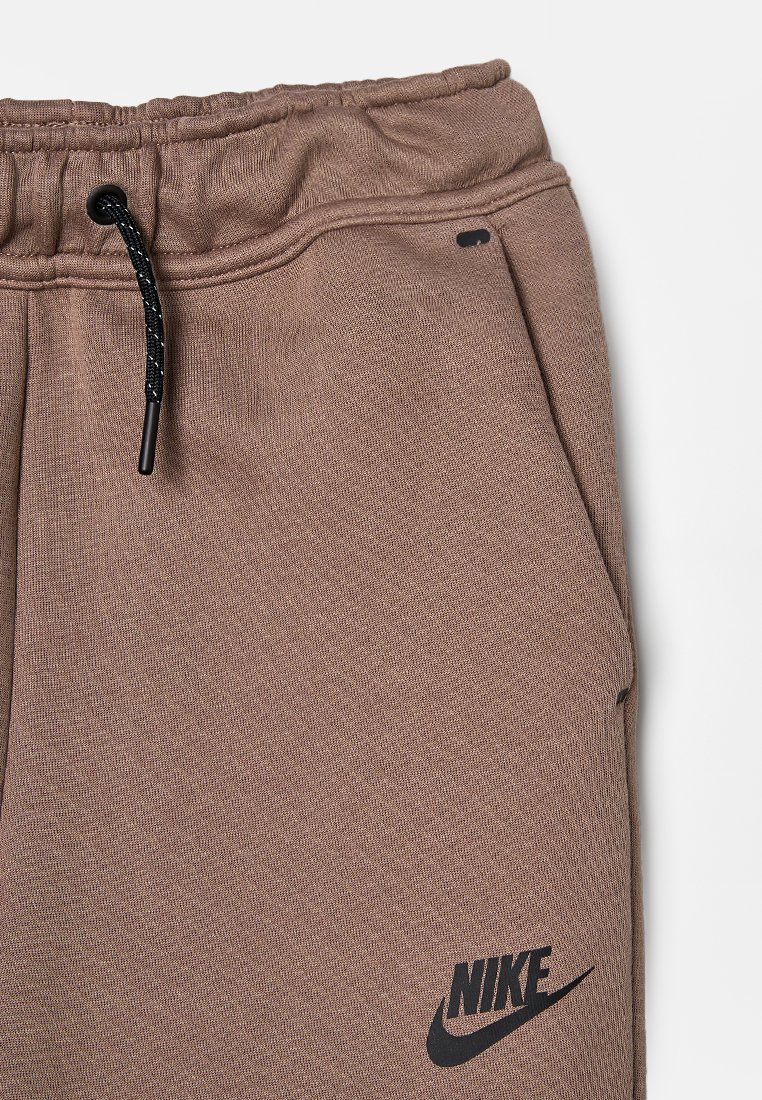 Sudadera marrón con textura, con cintura elástica y cordón. Incluye un logo negro de Nike en la parte baja de la pierna y un bolsillo lateral.