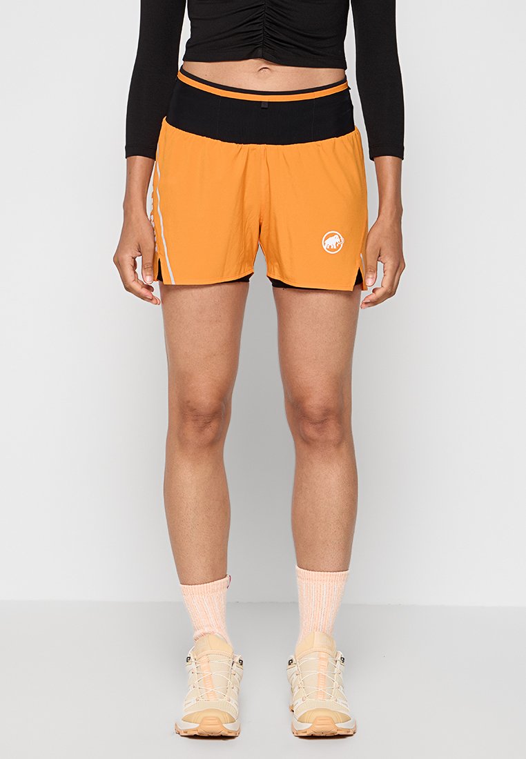 Pantalones cortos deportivos naranjas con una cinturilla negra, rayas laterales y logo. Tejido ligero, longitud por encima de la rodilla, con ligeras aberturas laterales.