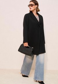 Sort frakke med reverskrave, båret over en beige top; parret med lyseblå jeans med bred ben og en struktureret sort håndtaske.
