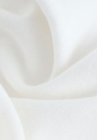Gros plan d'un tissu blanc doux avec une texture fine en maille et des plis doux créant des courbes lisses et des ombres.