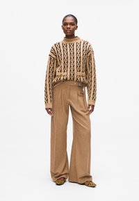 Beige strikkegenser med svart geometrisk mønster, kombinert med beige vidbukser. Akkompagnert av leopardmønstrete slip-on-sko.
