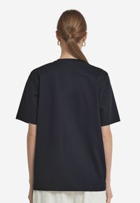 Marinblå bomullströja med korta ärmar och avslappnad passform, omgiven av rund hals och en mjuk textur. Bakifrån syns inga ytterligare detaljer.