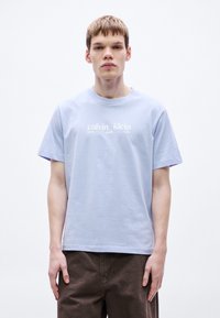 Svetlomodré bavlnené tričko s krátkymi rukávmi, okrúhlym výstrihom, s bielym nápisom „calvin klein new york city“ na prednej strane.