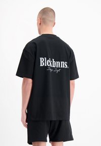 Zwarte oversized t-shirt van katoen, met witte geborduurde tekst op de achterkant: "Blckbnns Design Dept.", ronde hals, korte mouwen.