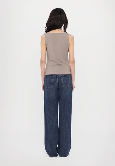 Brun uten ermer topp kombinert med løse, høyt liv blå jeans. Stoffet fremstår mykt, med en glatt tekstur og minimal detaljer.