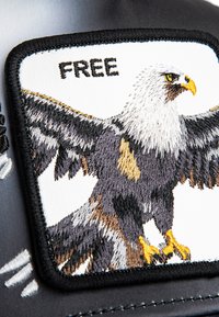 Tela negra con un parche bordado de un águila. El águila tiene una cabeza blanca y alas oscuras, con la palabra "LIBRE" encima en costura negra.