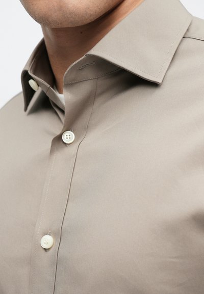 Beige button-up shirt with a smooth texture, featuring a classic collar and white plastic buttons along the front. Simple, tailored design.