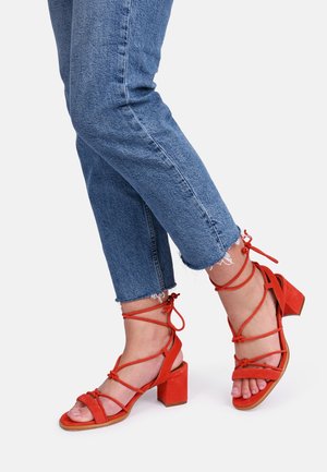 Røde ruskindssandaler med hæle, ankelstropper, firkantede tådele og blokhæle, kombineret med cropped blå jeans med frynsede kanter.