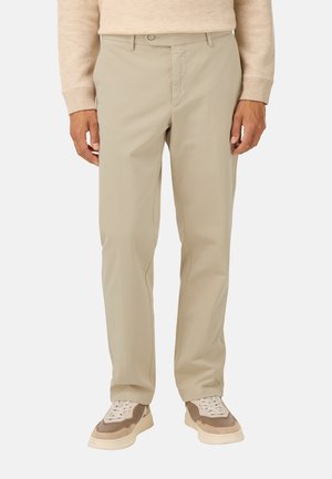 Pantalones rectos beige hechos de algodón con una textura suave. Cuentan con un cierre de botón y bolsillos laterales. Combinados con zapatillas marrones y crema.