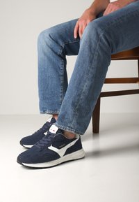 Zapatillas deportivas azul marino con acentos blancos, material de ante y malla, superficie texturizada, diseño con cordones y suela plana de goma.