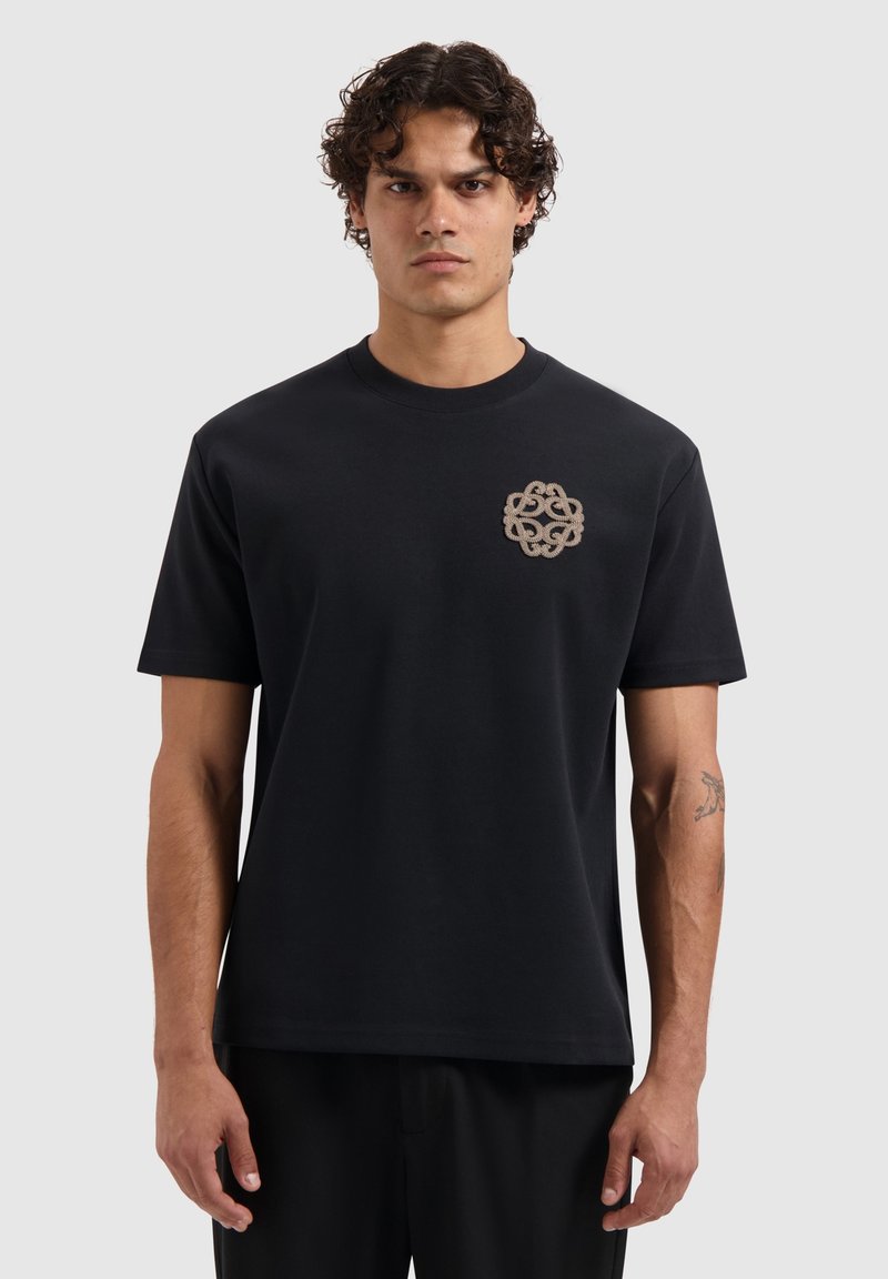 Zwarte katoenen t-shirt met korte mouwen en een ronde hals, met een ingewikkeld beige geborduurd patroon op de linkerkant van de borst.