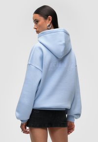Felpa oversized azzurro chiaro con cappuccio, stampa del logo testurizzata sul retro e maniche larghe; abbinata a una mini gonne in denim nera.