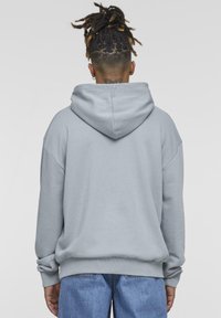 Grey hoodie with a large hood, loose fit, ribbed cuffs, and waistband. Soft texture, no visible patterns or designs.