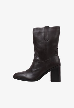 Bottine en cuir brun avec un bout carré, un talon carré haut et des détails cousus sur le côté, dotée d'une languette pour un enfilage plus facile.