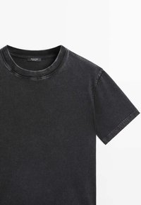 T-shirt nera a maniche corte realizzata in morbido cotone. Presenta un colletto a girocollo, una sottile texture sbiadita e cuciture visibili attorno al colletto e alle maniche.