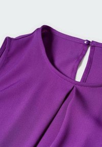 Blouse violette avec une ouverture en forme de trou de serrure à l'arrière, texture lisse, et détail plissé au niveau du col, confectionnée dans un tissu léger.