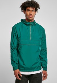 Teal hættejakke med en kvart-zip design, der har en frontlomme og elastiske manchetter. Fremstillet af glat, let materiale.