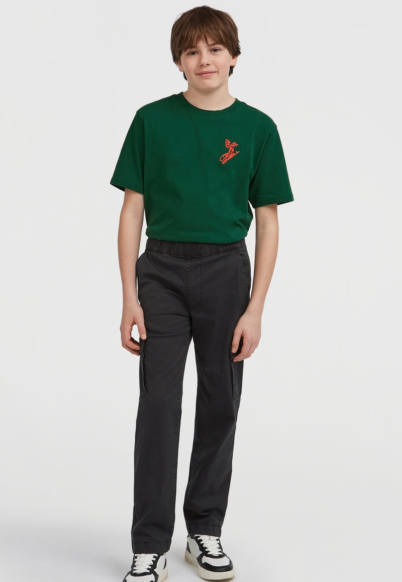 Grön bomullströja med en orange grafisk design, i kombination med svarta byxor med elastisk midja och sidofickor samt svarta och vita sneakers.