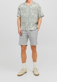 Camisa de manga corta, abotonada, en gris claro con un patrón de paisley blanco; combinada con pantalones cortos gris claro y zapatillas crema con acentos beige.