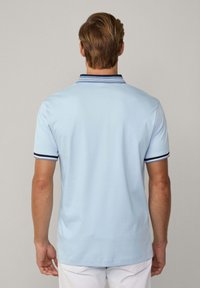 Světle modrá polo košile vyrobená z bavlny s úzkým střihem. Má tmavě modrý límec s bílými pruhy a krátké rukávy.