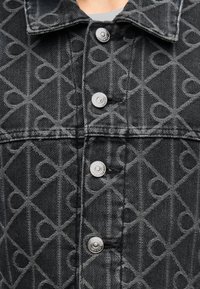 Μαύρο τζιν μπουφάν με διακριτικό γεωμετρικό σχέδιο, ασημί κουμπιά τύπου snap και υφή με ανάγλυφο φινίρισμα.