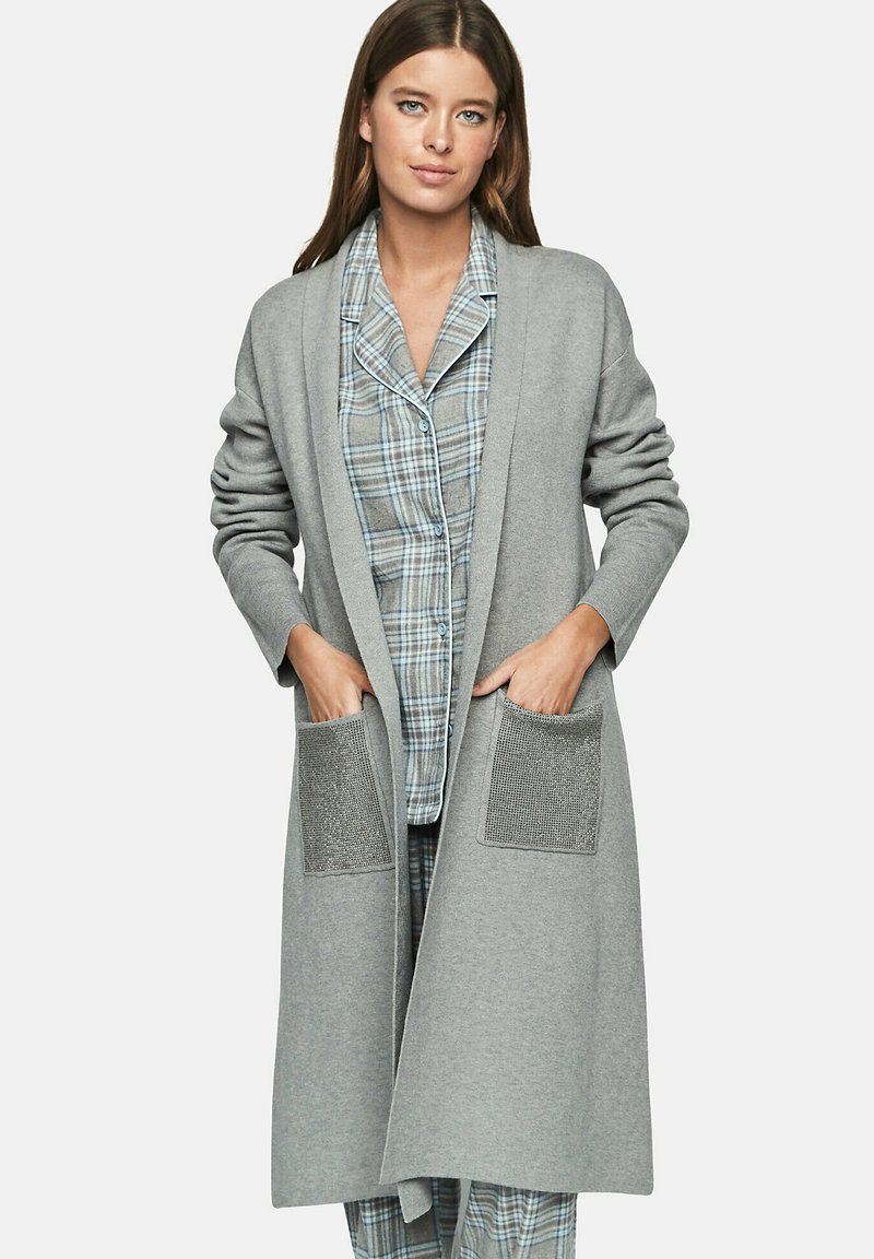 Cardigan long gris avec un devant ouvert, en tissu doux, doté de deux poches à patch texturées. Porté par-dessus un ensemble de pyjama à carreaux bleus.
